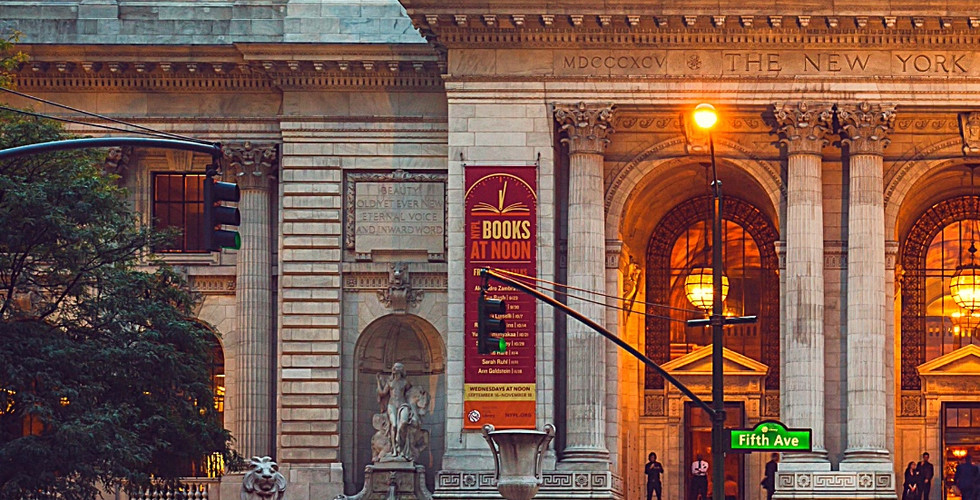 New York Public Library façade at dusk, street scene with blurred motion of pedestrians and cars, bright orange cones, and lit signs.