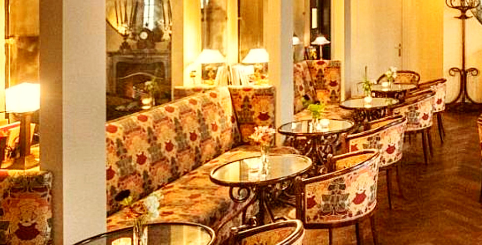 Elegant restaurant with floral patterned chairs, mirrored walls, and warm lighting. Text: "Hotel Locarno Dining, Rome, Italy." Cozy ambiance.