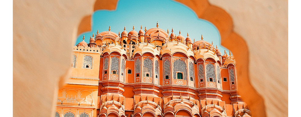 Ornate pink facade of Hawa Mahal in Jaipur framed by an arch. Clear blue sky. Text below reads "JAIPUR", latitude and longitude given.