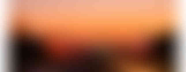 The image shows Rashtrapati Bhavan in New Delhi at sunset. Illuminated buildings glow against an orange sky, with a road leading to the horizon.