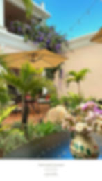Terracotta courtyard with plants, umbrellas, and flowers. Wisteria drapes from balcony. Clear sky. Text: Ojala Hostel Courtyard, Antigua.