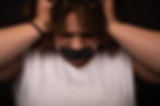 Slightly blurred close up of Kate Robinson with black tape covering her mouth looking down with her hands on either side of her head
