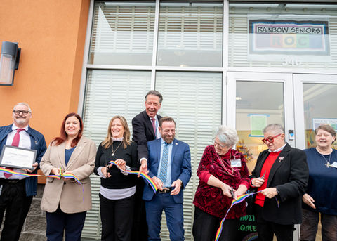 A diverse group of people participating in a ribbon-cutting ceremony to inaugurate the grand opening of a Rainbow Senior, Inc. in Rochester, NY