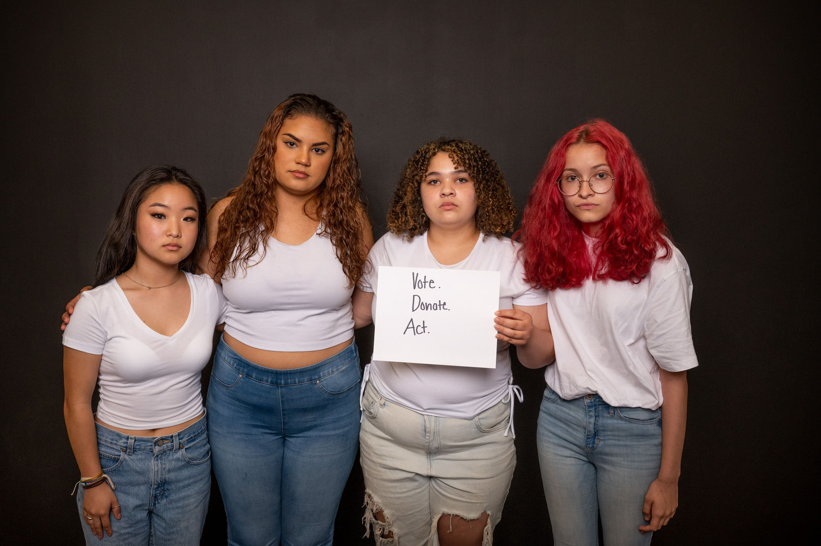 a group of four students each wearing a white t-shirt and jeans looking at the camera holding a sign that says, "Vote. Donate. Act.: