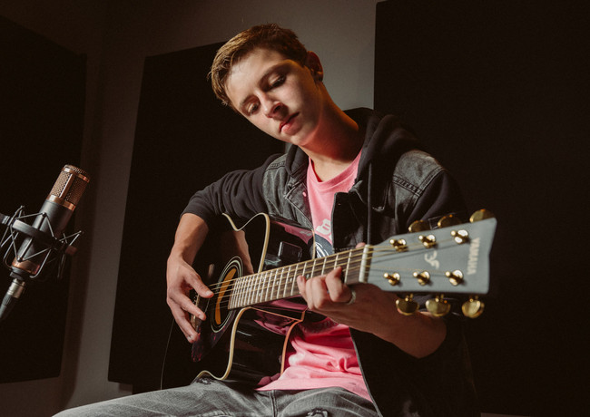 high school senior boy playing guitar in a recording studio