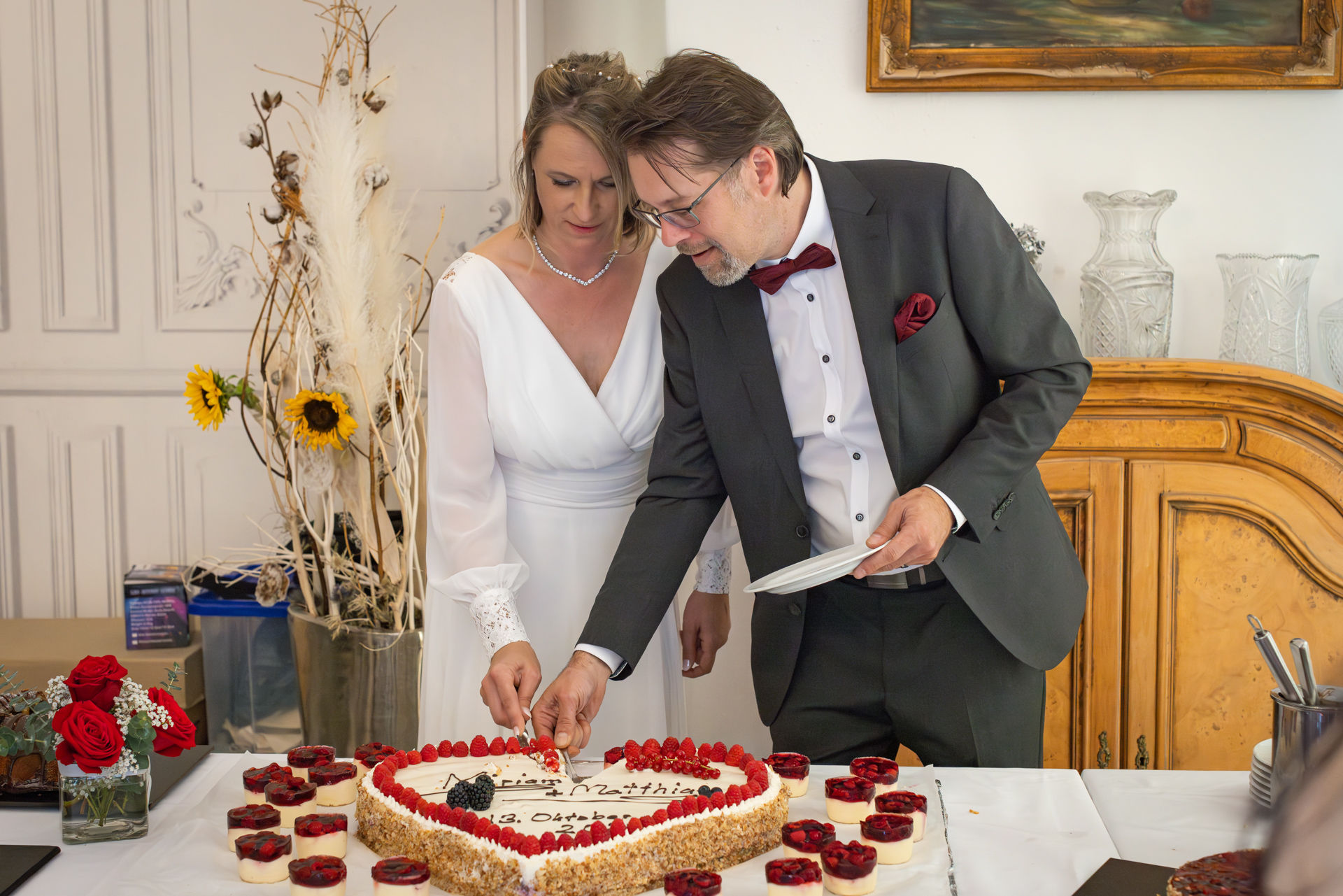 Fragen an den Hochzeitsfotografen, Hochzeitstorte in Herzform mit Himbeeren, Braut und Bräutigam schneiden an