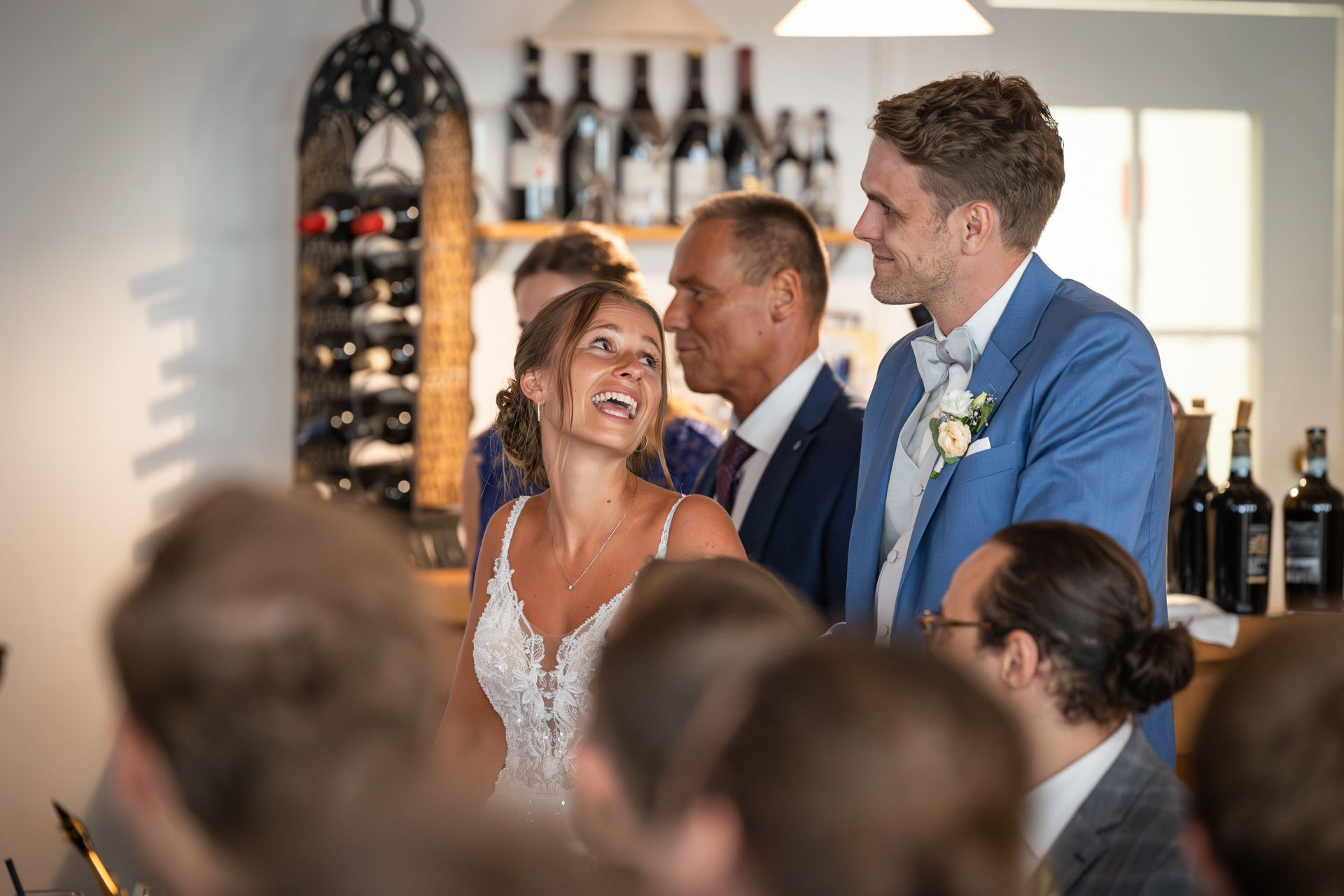 Braut lacht Bräutigam an, im Hintergrund Weinregal