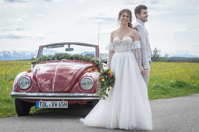 Braut und Bräutigam stehen an roten VW Käfer Cabrio