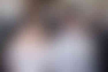 Braut und Bräutigam sitzen, Braut schaut Bräutigam an, Bräutigam lacht, im Hintergrund Gäste