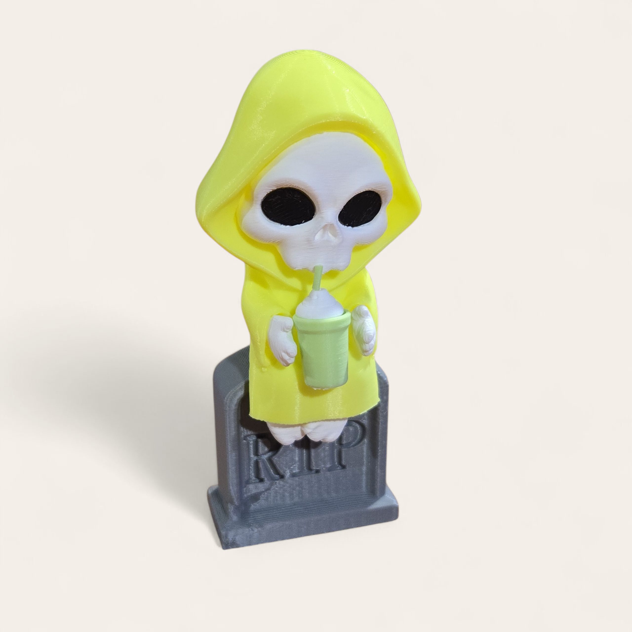 Cartoon skeleton figurine in yellow hood drinking from green cup