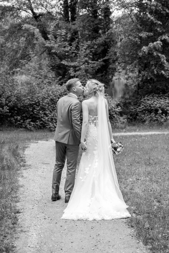 Ein Brautpaar küsst sich auf einem Weg; Hochzeit im Freien mit Bäumen.