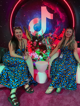 The Sugarcoated Sisters sitting at the TikTok lounge during VidCon LA surrounded by neon décor.