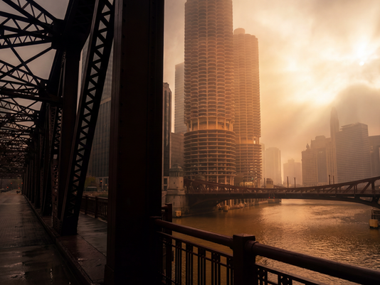 Chicago skyline viewed from a bridge at golden hour with dramatic clouds.