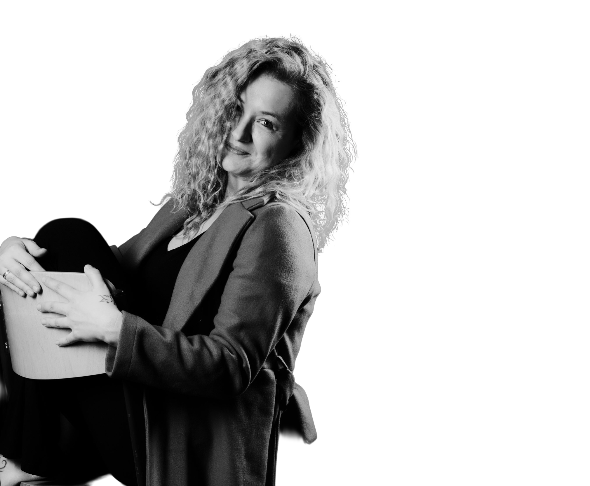 Person mit lockigem Haar in Schwarz-Weiß, Portraitaufnahme vor dunklem Hintergrund.