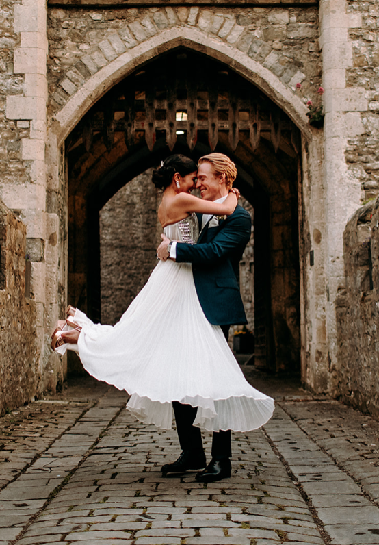 Groom lifting his bride in front of a castle entrance.