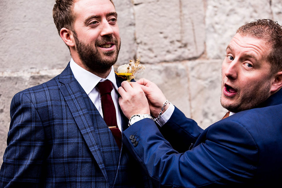 Groomsman helping a groom with his buttonhole.