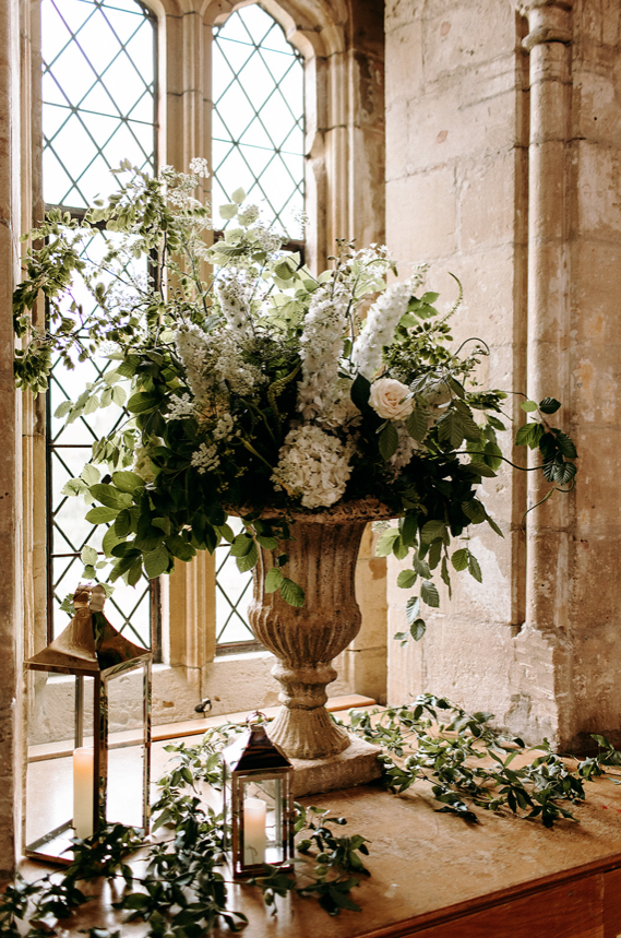 Green and white floral displays in a large stone urn.