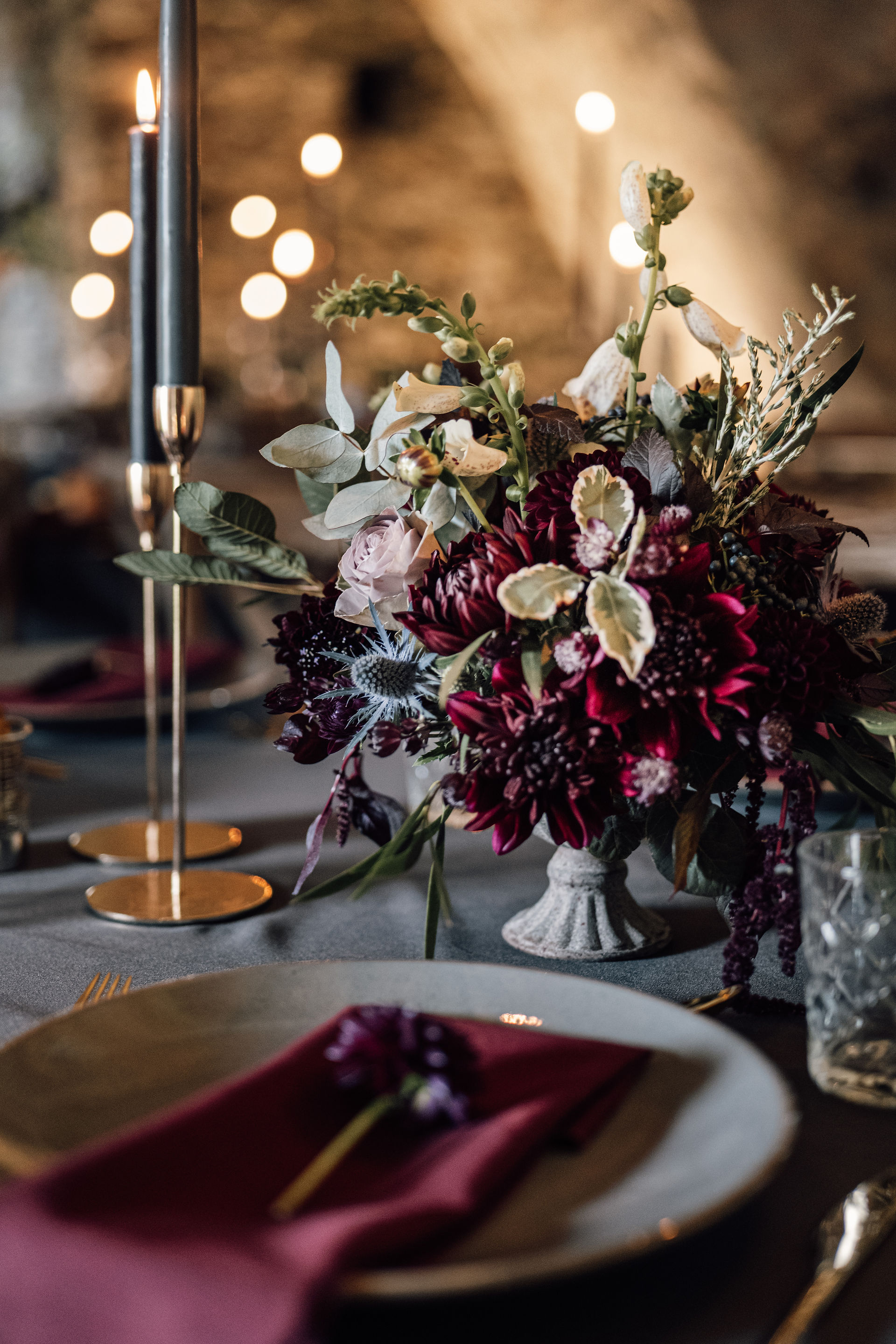 Wedding table dressed with tall grey candles in gold candle sticks, charcoal linen and large flower displays in autumnal colours.