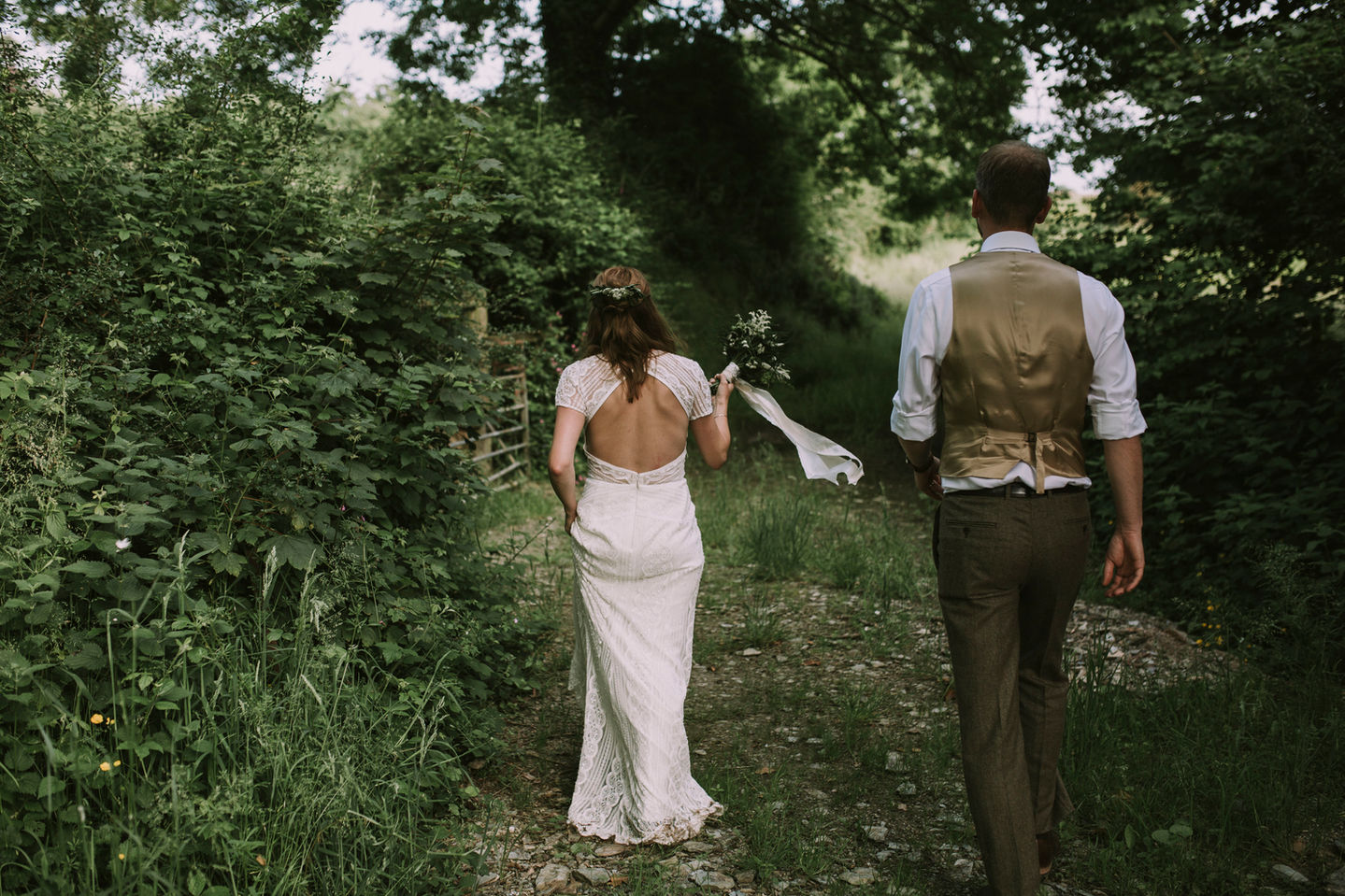Couple shot of a bride and groom walking away down a wild verge.