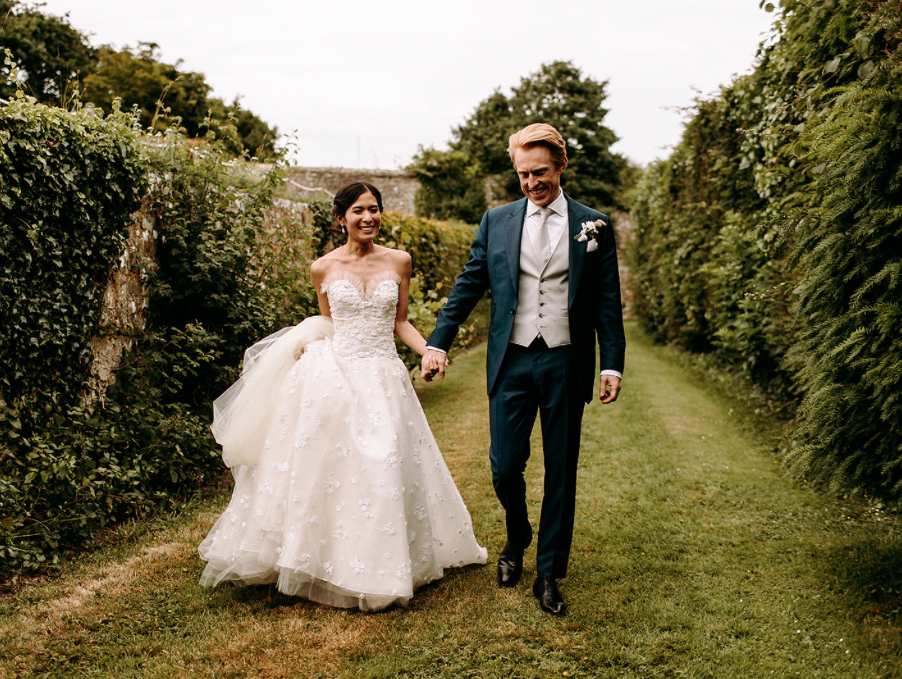 Bride and groom walking hand and hand through castle gardens.