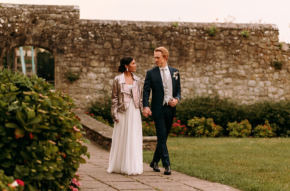 Bride and groom walking hand in hand through castle gardens.