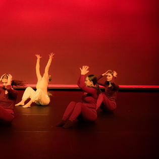 One dancer with both hands raised toward the sky while others hold their head in their hands. 