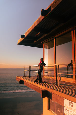 Woman watches sunset from a wooden deck overlooking the ocean view.