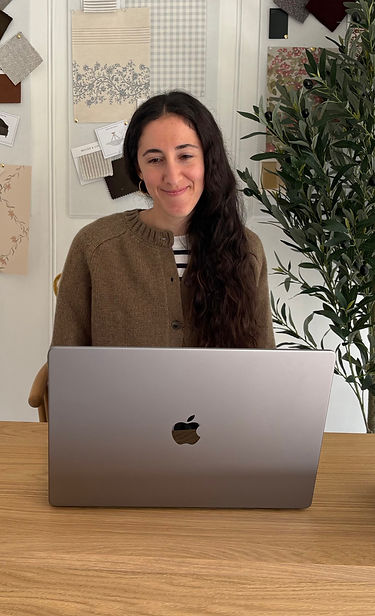 Camila, founder and interior designer of Camila Interiors, working on her laptop in her design studio, surrounded by fabrics