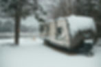 Travel trailer placed near river in winter forest in daylight by: Erik Mclean