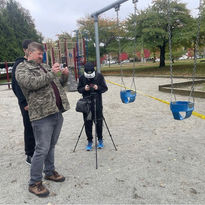 A man taking photos in a playground swingset, park background, Production Stills