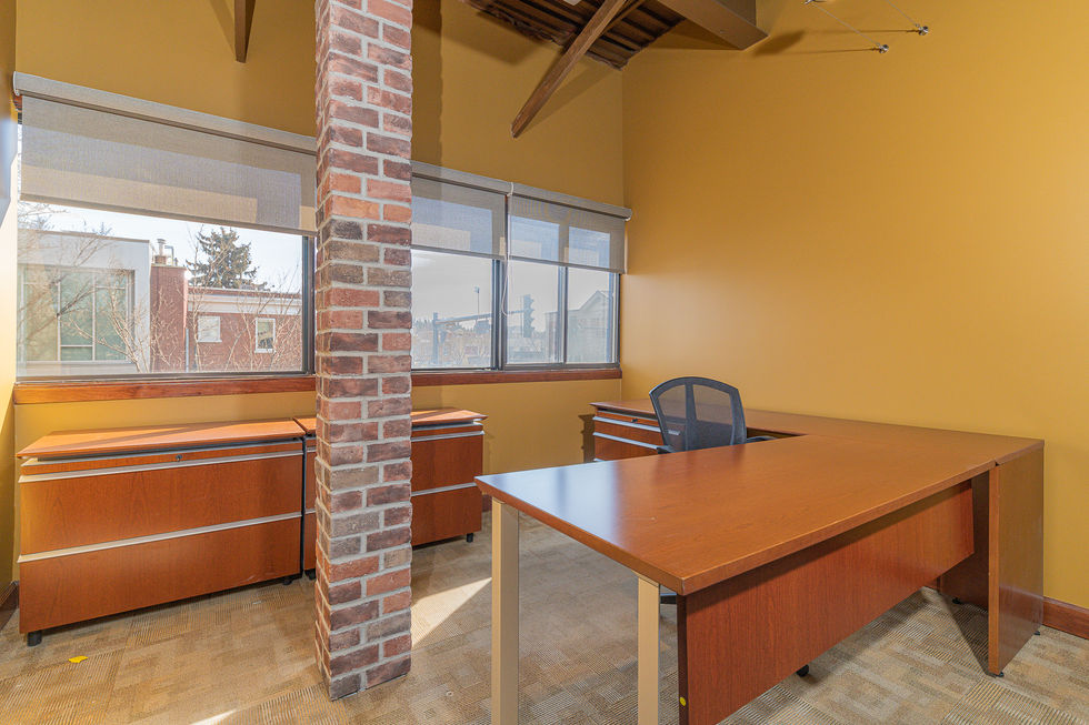 Office desk and file cabinet with a brick pillar right in the middle, large office window in the background