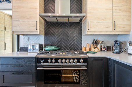 stunning luxury gas stove, elegant dark tile behind stove, sand coloured cabinets above the white granite counter, dark blue grey counters below
