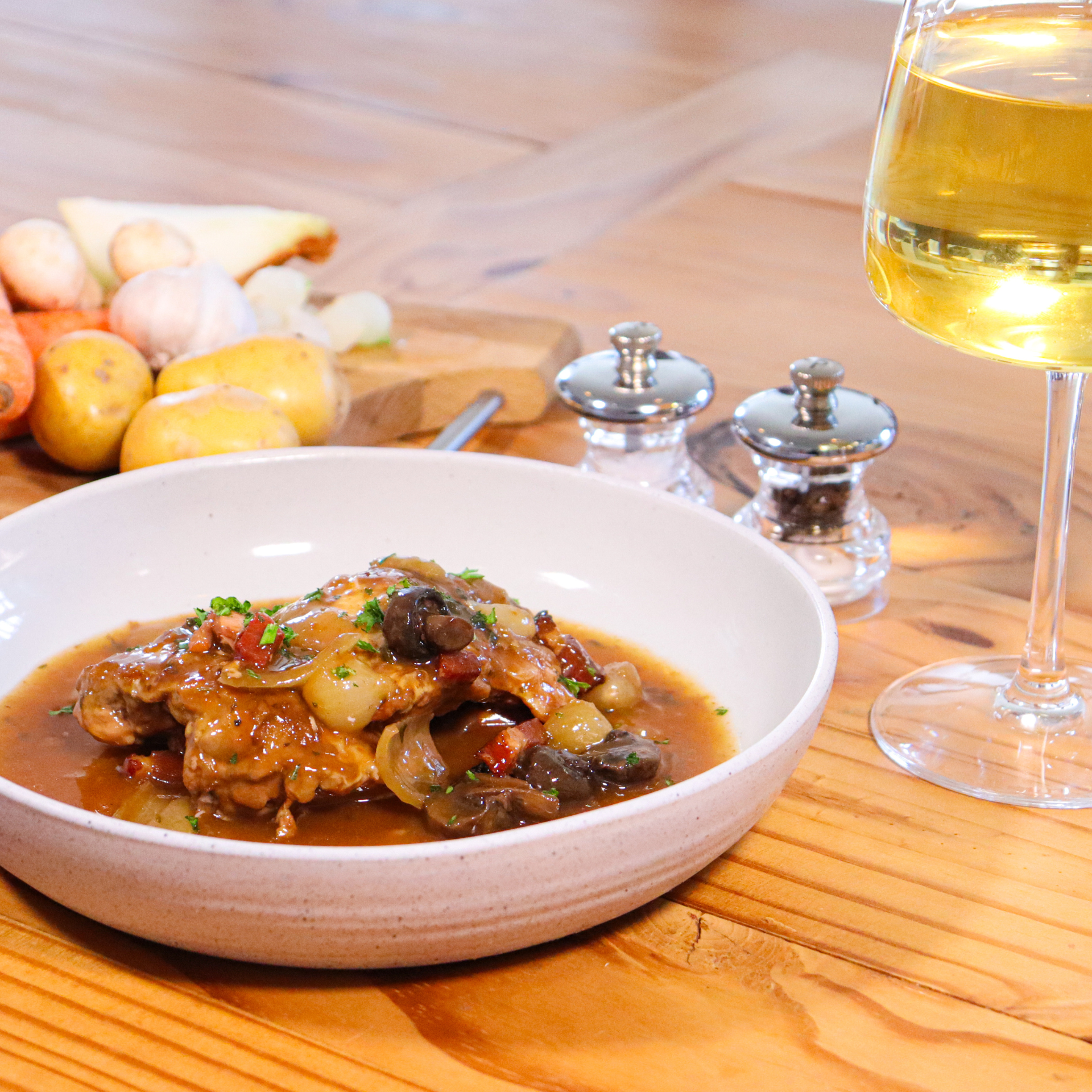 Coq au vin in a white bowl with a glass of white wine