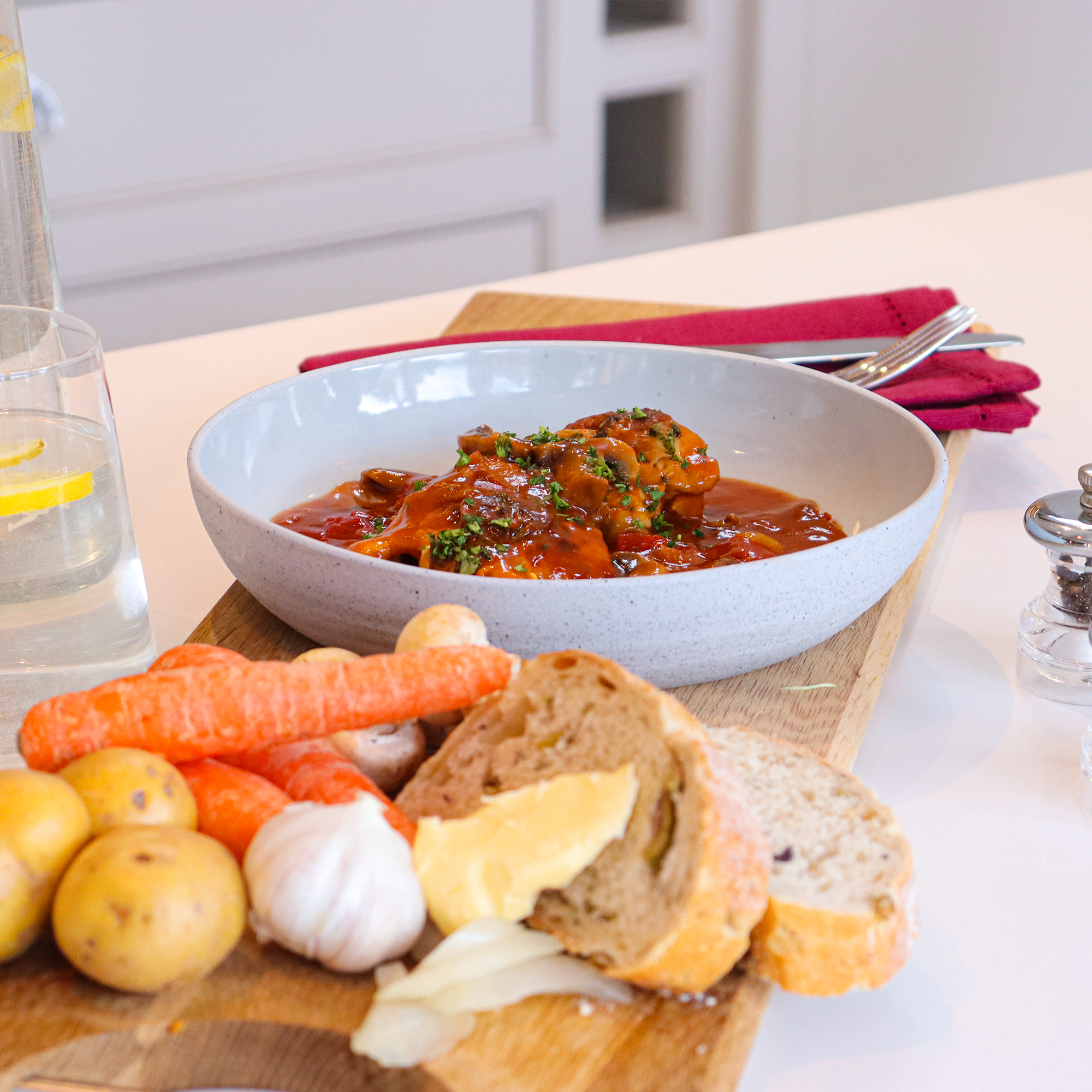 Chicken chasseur on a wooden board with crusty bread, carrots and garlic