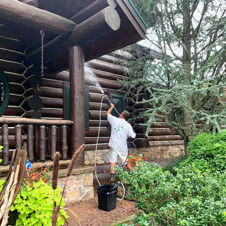 Man with power washer cleans a log cabin.