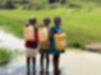 Three Kenyan children in a rural area standing in unclean water. Each holding a jug to fill with the water.