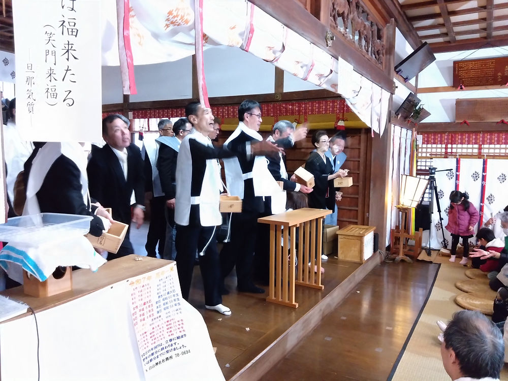 福来たろうの横断幕の下、豆まきをする男性たち。
