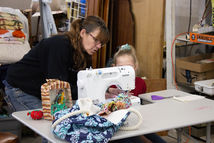 A person teaching a child at a sewing maching