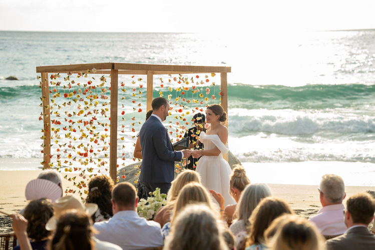 Beach wedding ceremony: couple exchanging vows, flower backdrop
