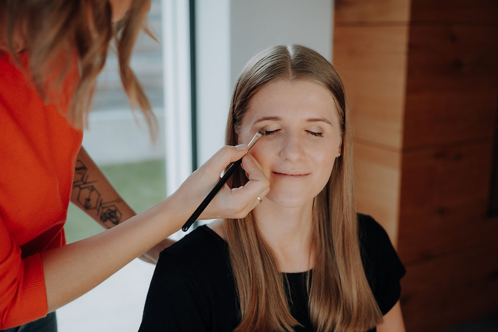 Eine junge Damen mit langen braunen Haaren wird von einer anderen Dame am Auge geschminkt