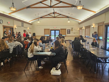 Students from the University of Missouri gather with community leaders inside the Rothwell Park Lodge in Moberly, seated at long tables during a collaborative workshop session, with presenters speaking at the front of the room.