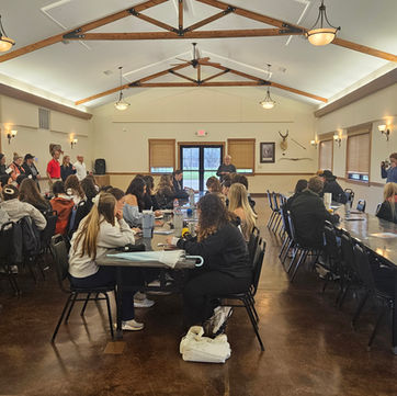 Students from the University of Missouri gather with community leaders inside the Rothwell Park Lodge in Moberly, seated at long tables during a collaborative workshop session, with presenters speaking at the front of the room.