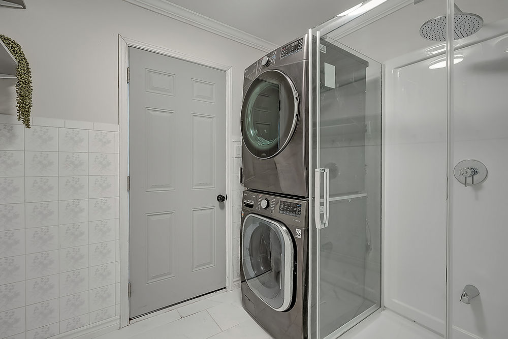Stacked washer and dryer unit next to a glass shower stall