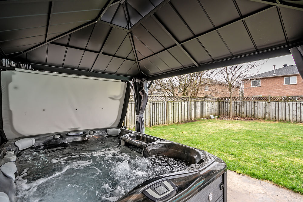 Bubbling hot tub under a black gazebo in a backyard