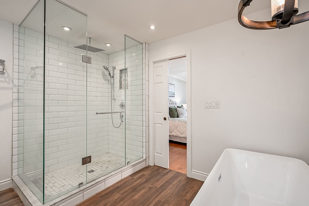 Modern bathroom with glass walk-in shower, subway tile, wood floor.