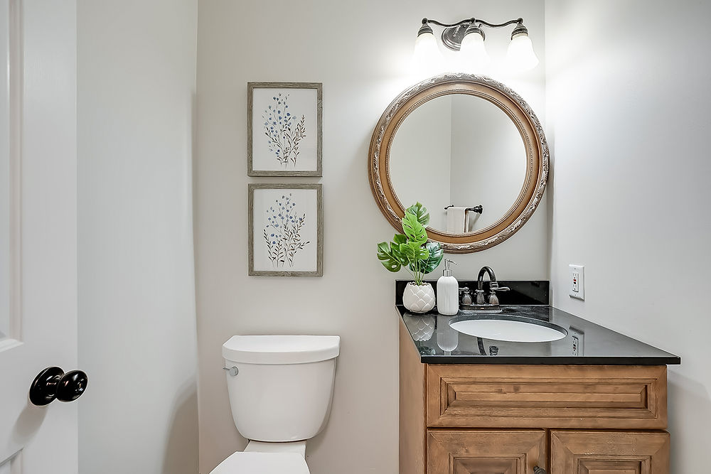 Powder room with white toilet, wood vanity, and round mirror