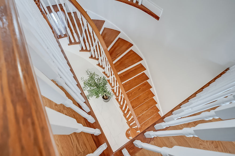 Winding wooden staircase with white railings, plant at base