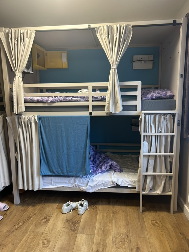 Bunk bed with beige curtains, teal bedding, and white shoes on light brown laminate floor.