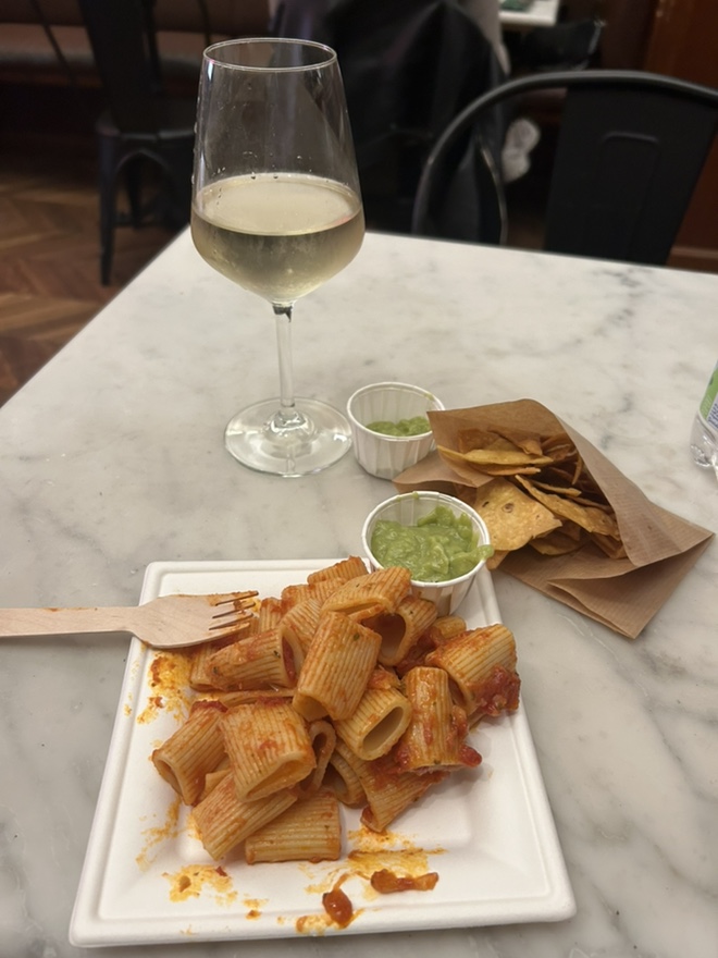 Pasta dish with tomato sauce, a glass of white wine, guacamole, and tortilla chips on a marble table.