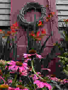 Echinacea and Crocosmia in front of a weathered red door with a wicker wreath